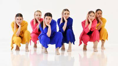 emme dance collective dancers crouching in colorful suits on a white background