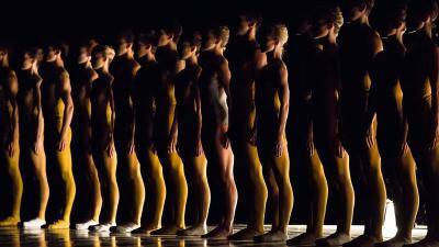 Silhouette of a line up of dancers wearing yellow unitards, in William Forsythe's "Artifact Suite",
