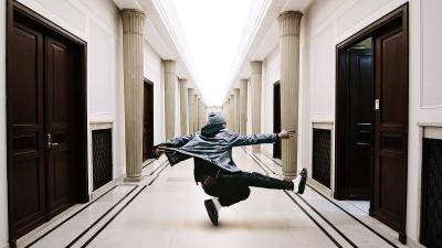 Male hip-hop dancer in the middle of a long hallway, pointing at an open door.