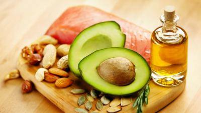 Half cut avocado, nuts, piece of fresh salmon, and a bottle of oil displayed on a small wooden board