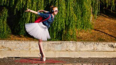 young dancer on pointe in a white tutu, jean jacket, and a red backpack