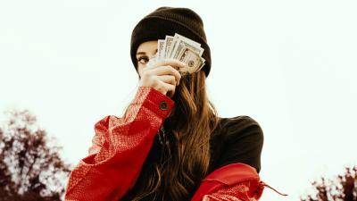 woman with black beanie and red leather jacket holding money in front of her eye