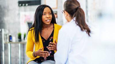 Black woman wiearing a yellow cardigan speaking to a doctor.