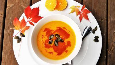 pumpkin soup in a white bowl and plate decorated with orange slices and fall color leaves