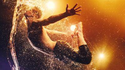male dancer jumping arching back splashing into water on an amber lit background