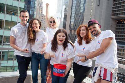 6 Broadway artists wearing a white t-shirt pointing at a small red bucket to collect money for Broadway Bares