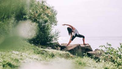 Young woman in a yoga pose on a flat rock in the middle of greeneries