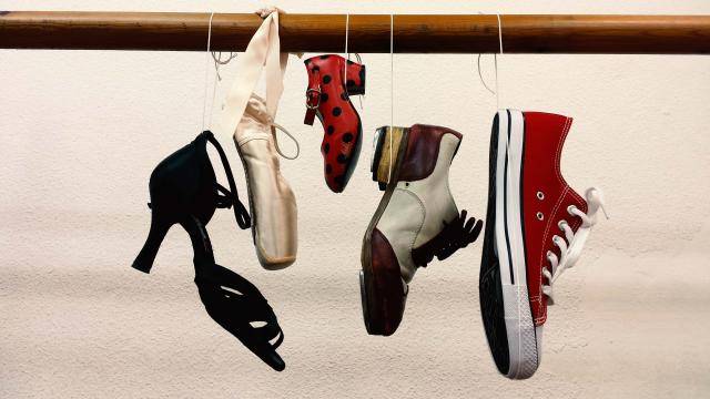 Different styles of dance shoes hanging off a wooden barre