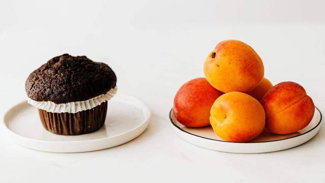 A chocolate cupcake one one place, a stack of peaches on the another place