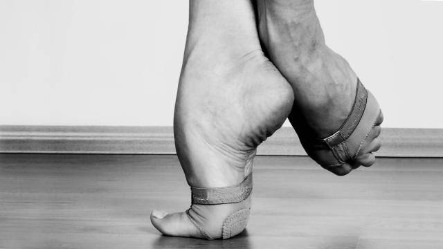 Close up of a dancer's feet on relevé with one foot pointed in a coupé position.