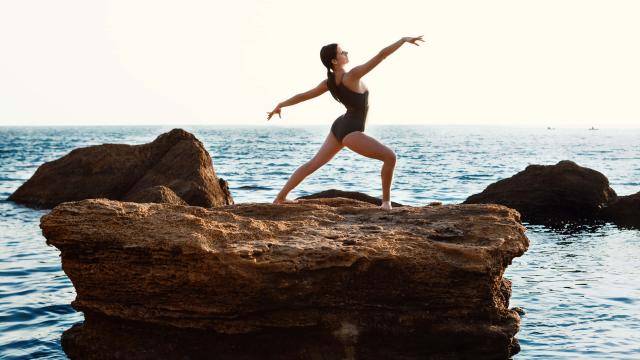 Female dancer posing in a lunge on a big rock against the ocean