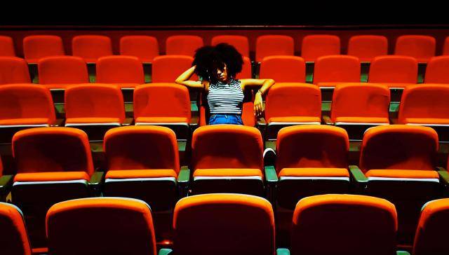 Young woman with an afro, sitting in the middle of empty seats of a theatre house.