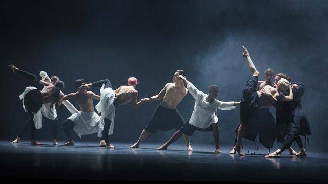 company Wayne Mcgregor artists in a stretched line, all in various poses, foggy atmosphere on stage
