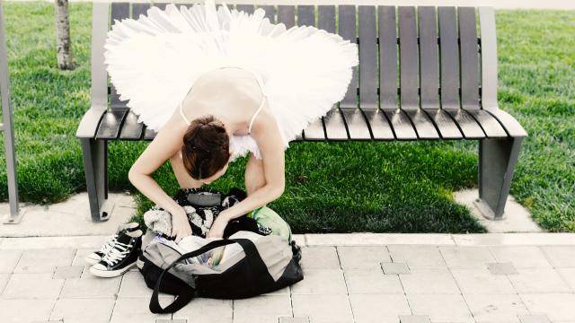 young ballerina sitting on a bench leaning over looking into her bag