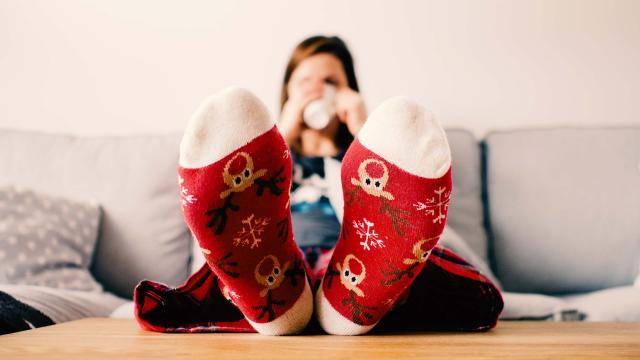 young woman sipping hot drink on couch with holiday themed socks