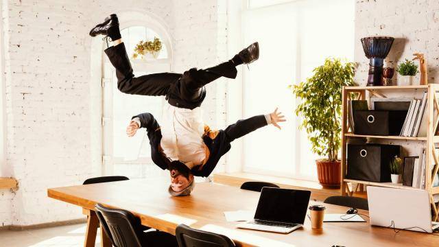 Breakdancer in a suit spinning on his head on an office desk