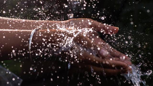 Close up of hands cupped together under falling water