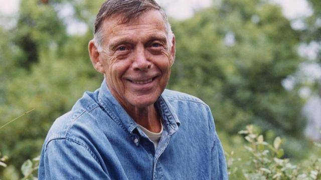 Paul Taylor in a jean shirt, smiling at camera, on a greenery background